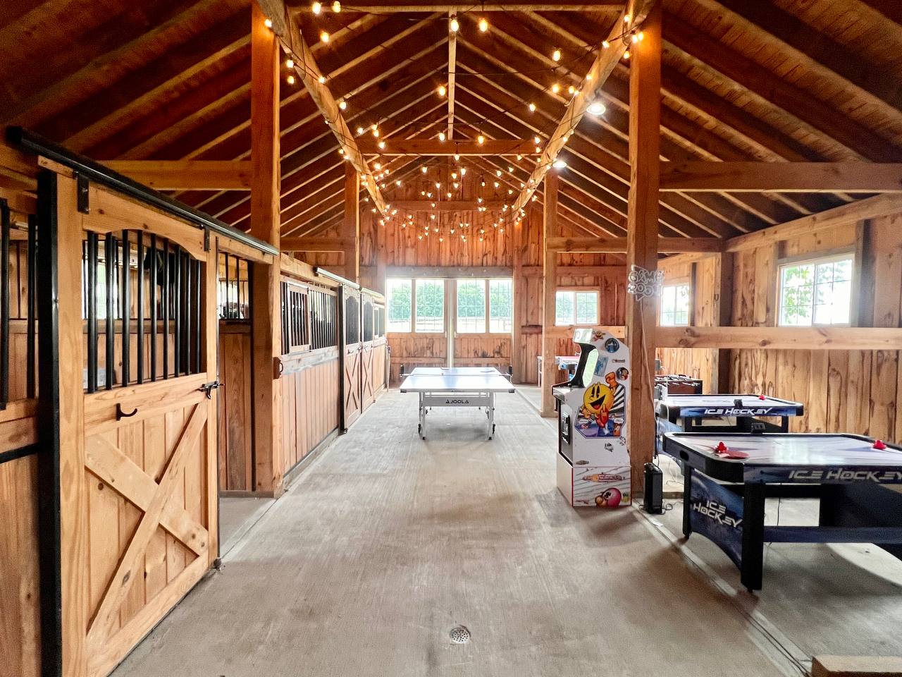 Barn game room at The Westtown Reset with ping pong table, Pac-Man arcade, air hockey, and string lights — private estate entertainment upstate New York