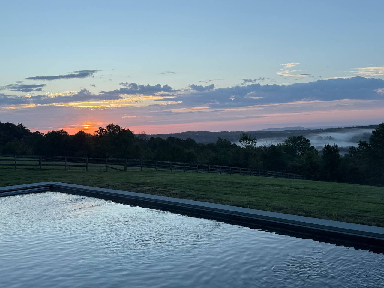 Heated pool at The Westtown Reset at sunrise with morning fog over the Hudson Valley hills — private estate retreat upstate New York